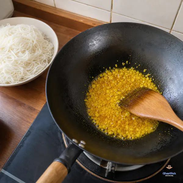 Garlic and yellow curry powder bubble gently in vivid golden oil over low heat while drained white rice vermicelli waits beside the wok
