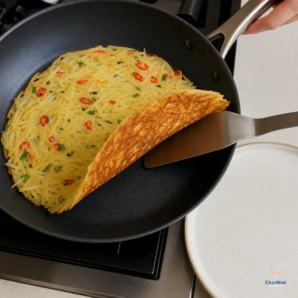 A spatula lifts the edge of an intact thin potato pancake to reveal an evenly deep-golden underside, with a plate ready beside the skillet