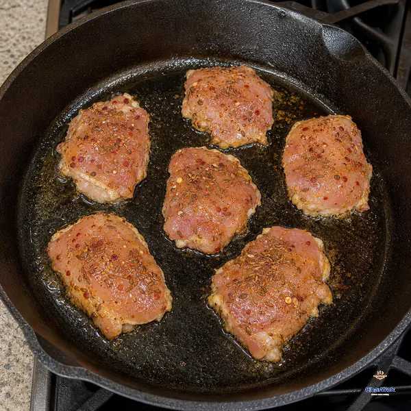 Exactly six cumin-and-chilli-coated boneless skinless chicken thighs sear flat with space between them in a dry cast-iron skillet