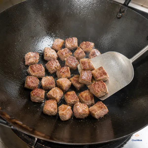 Even 2 cm lamb cubes with deep-golden contact faces sear in one loose layer while a wok spatula begins lifting them out