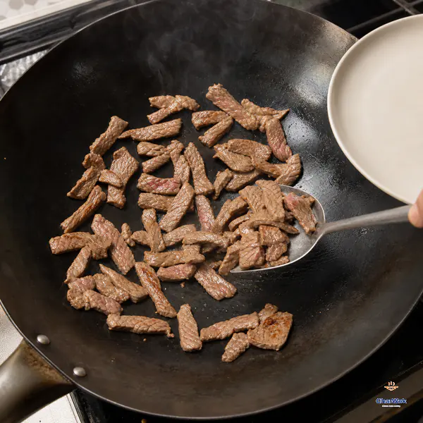 Thin beef strips sear with clear gaps in a hot wok while a spatula lifts out pieces whose outsides are pale brown and thicker centers remain slightly pink