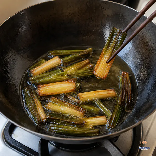 Chopsticks lift a split scallion section from gently bubbling oil when its white portion is deep golden amber and its green portion is dark jade-brown