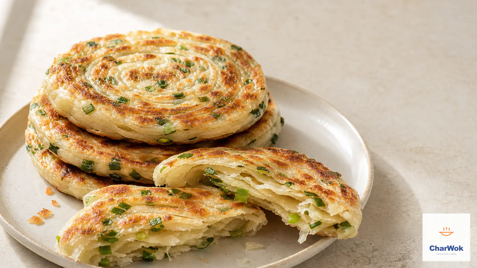 Four golden-brown Chinese scallion pancakes with visible spiral layers on a ceramic plate, with one torn open to reveal the flaky scallion-filled center