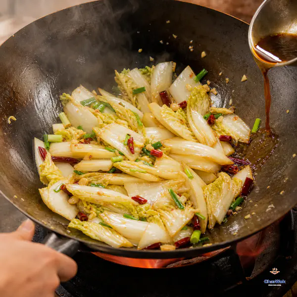 A thin stream of premixed sauce hits the exposed hot wok edge beside just-wilted Napa leaves and thick crisp-looking white ribs