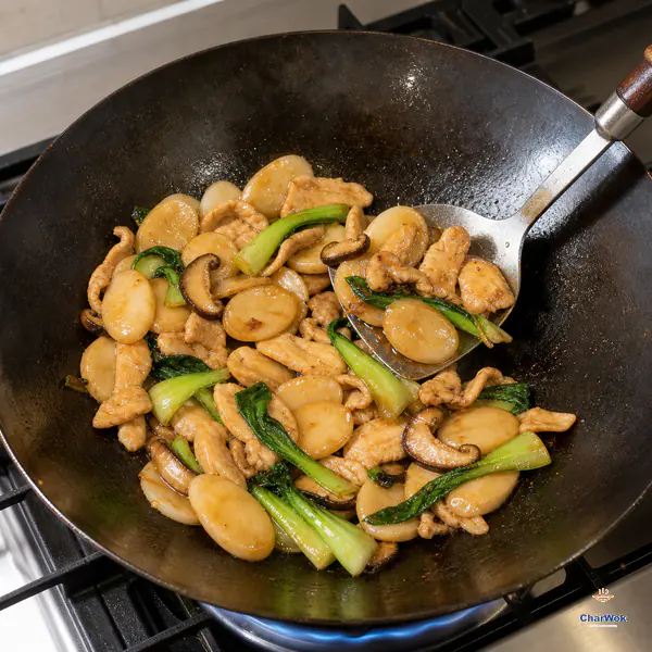 A wok spatula turns separate rice-cake slices, chicken, bok choy and shiitake in a thin glossy soy glaze with almost no free liquid on the exposed wok