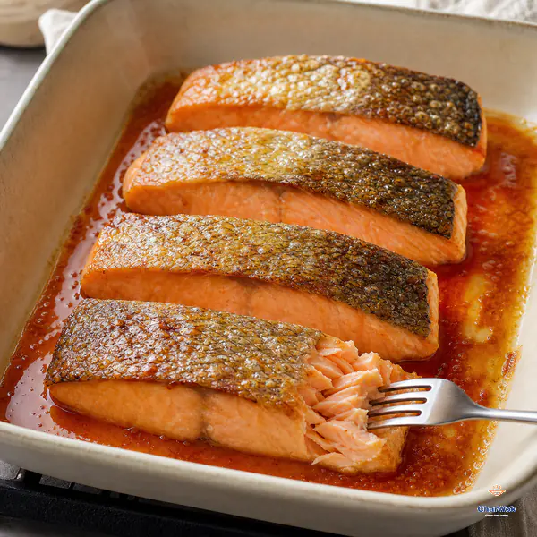 Four broiled salmon portions have golden blistered skin while a fork nudges one side into moist clean flakes above a little glossy reduced sauce