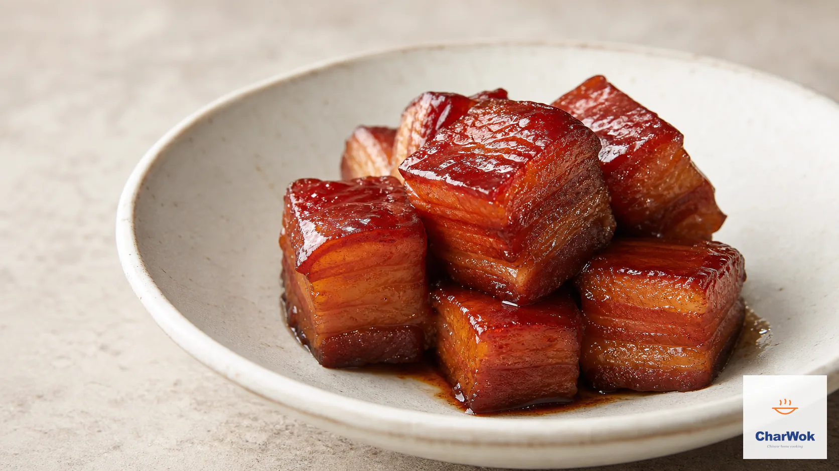 Chinese red-braised pork belly with glossy red-mahogany skin-on cubes, distinct skin, fat, and lean layers, and a thin clinging glaze in a warm-white bowl