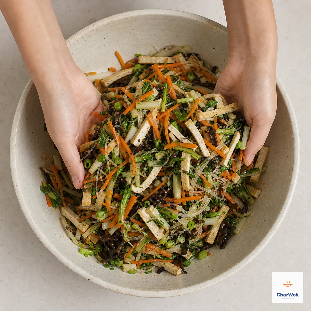 Hands mix a loose dry filling of bok choy, carrot, pressed tofu strips, shiitake, wood ear, and short glass noodles with no liquid pooling below